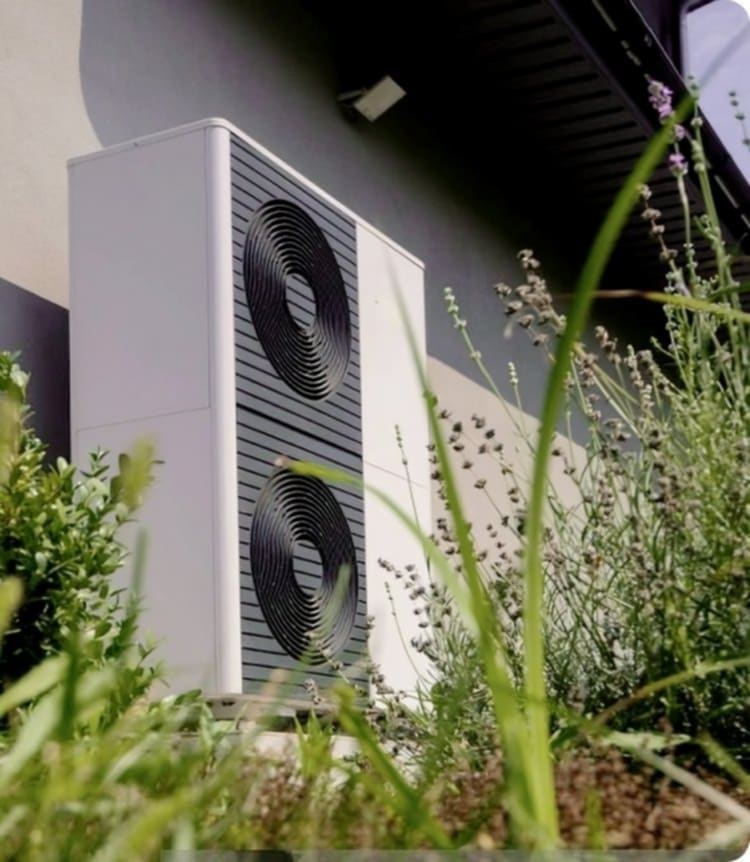 Une PAC air-eau installée à l'extérieur d'une maison avec de l'herbe devant